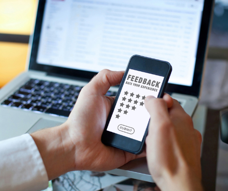 Image depicting a person working on a laptop and leaving feedback on a phone.