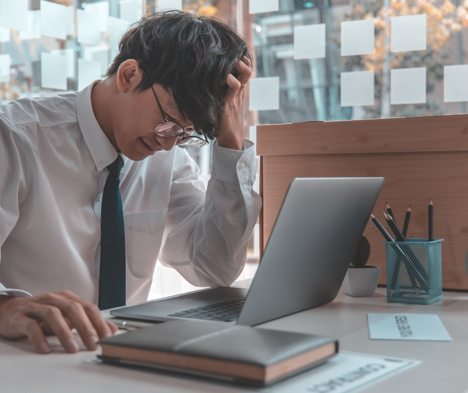 Picture of someone working at a desk looking frustrated at the laptop.